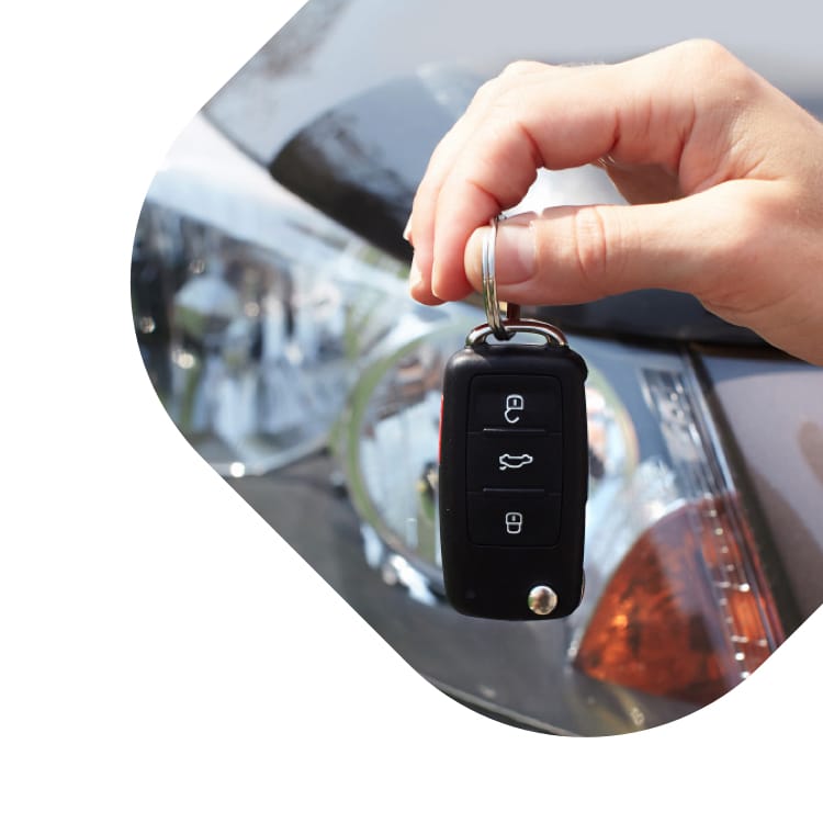 A set of car keys being held in front of a used vehicle.