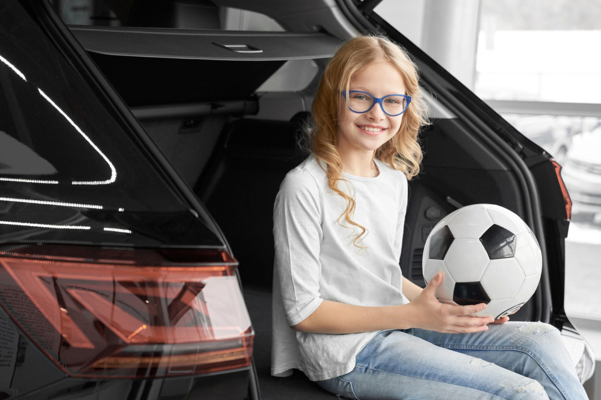 Young girl sitting in trunk of a trade-in vehicle with a soccer ball.